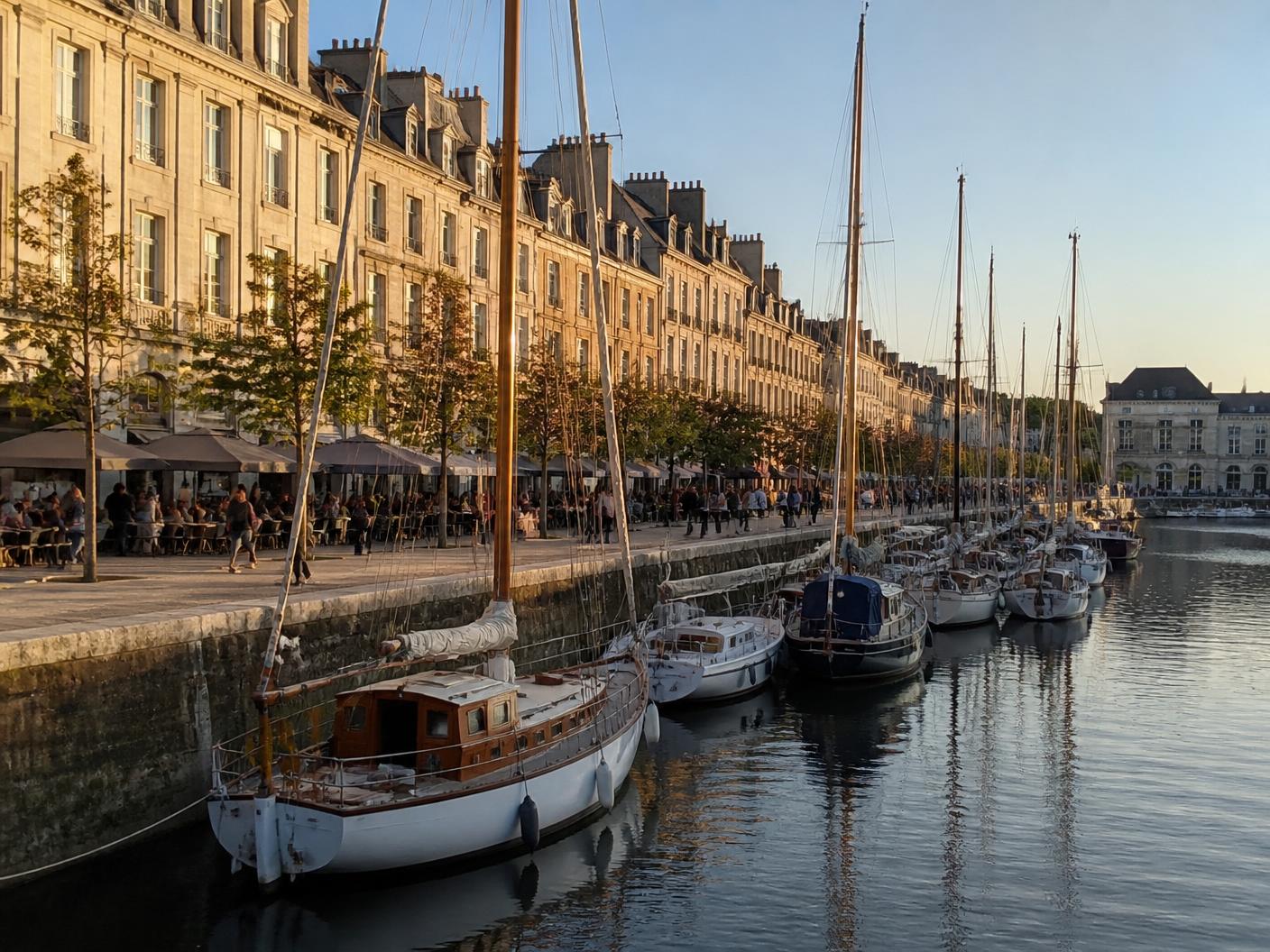 Illustration du bassin Saint-Pierre à Caen : voiliers amarrés, quais animés et immeubles de pierre claire