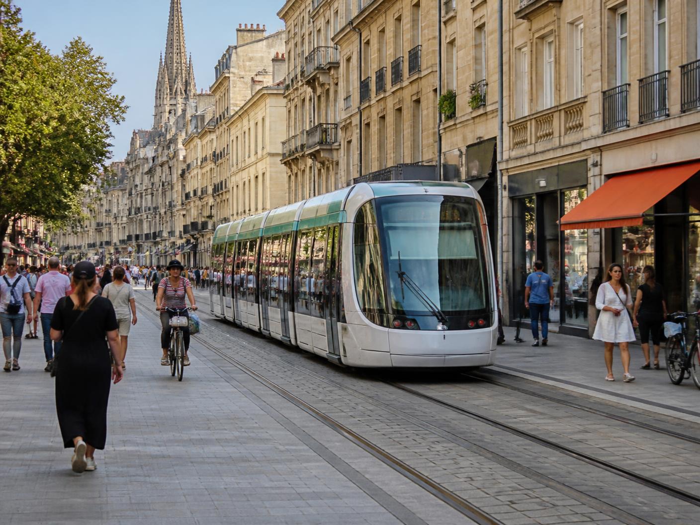 Illustration du tramway de Caen dans le centre : rame moderne, façades de pierre claire et voyageurs