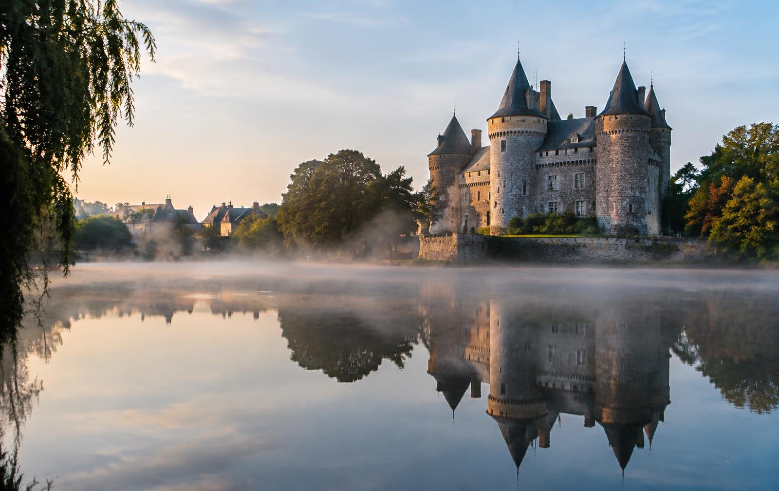 Château de Combourg et son lac, tours de granit et arbres reflétés dans l'eau