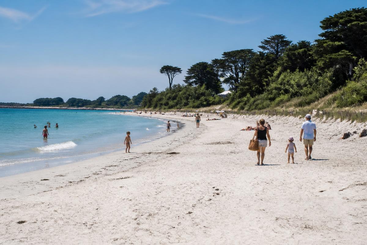 Plage de sable clair près de Concarneau : eau turquoise, pins et promeneurs