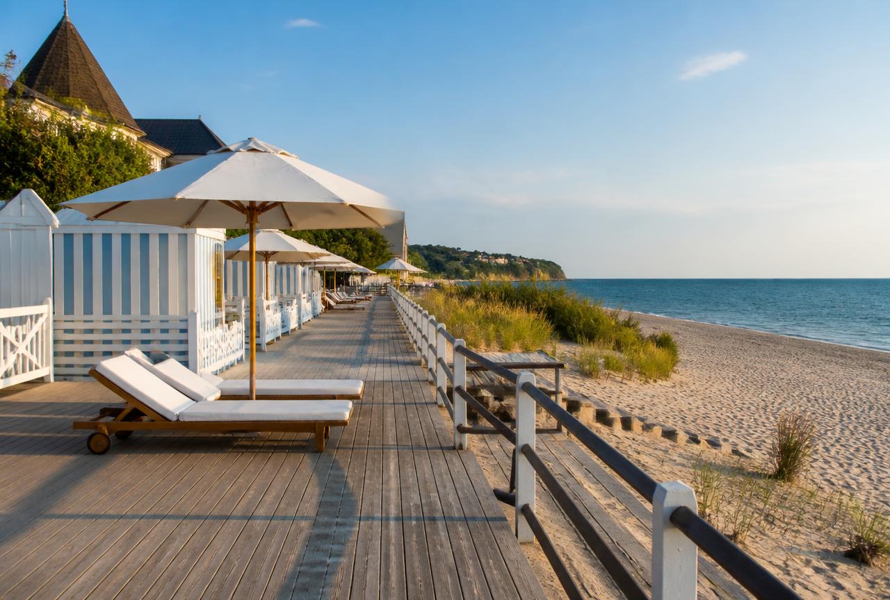 Illustration des planches de Deauville : promenade en bois, parasols blancs et plage de sable
