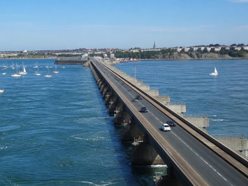 Illustration du barrage de la Rance : chaussée franchissant l'estuaire, voiliers au mouillage et ville au loin